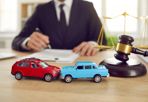Toy cars in a collision next to a gavel and scales of justice, illustrating a lawyer handling a car accident claim.
