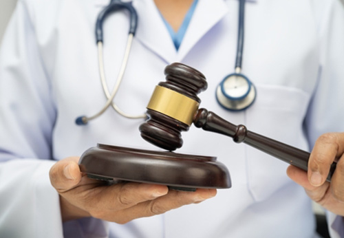 Doctor in lab coat and stethoscope holding a gavel, symbolizing medical malpractice or law