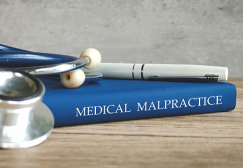 Close-up of a blue book titled MEDICAL MALPRACTICE with a stethoscope and pen on top.