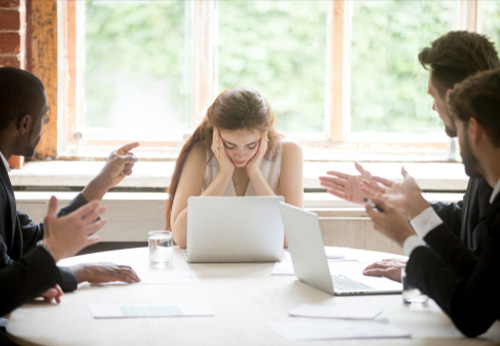 Distressed woman at a meeting while colleagues argue; representing a hostile work environment.